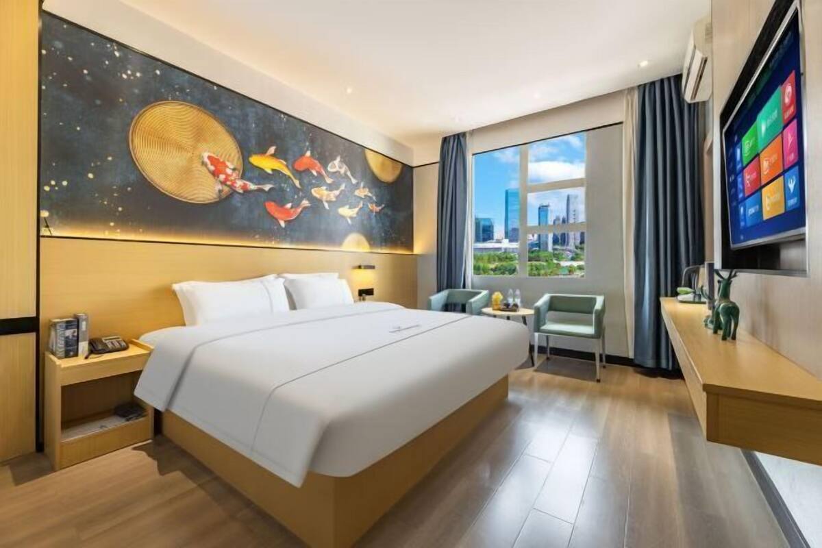 A modern hotel room with a large bed, a desk, a chair, a TV, and a city view.