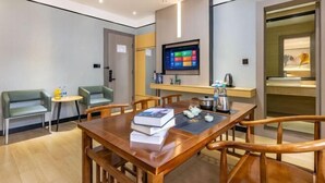 Una habitación de hotel moderna con una mesa de comedor de madera, dos sofás verdes, un televisor de pantalla plana y una pequeña cocina.