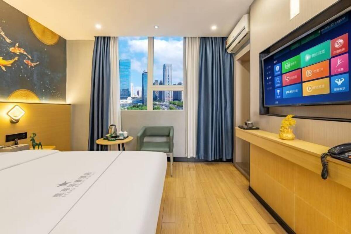 A hotel room with a bed, a desk, a TV, a window with curtains, and a city view.