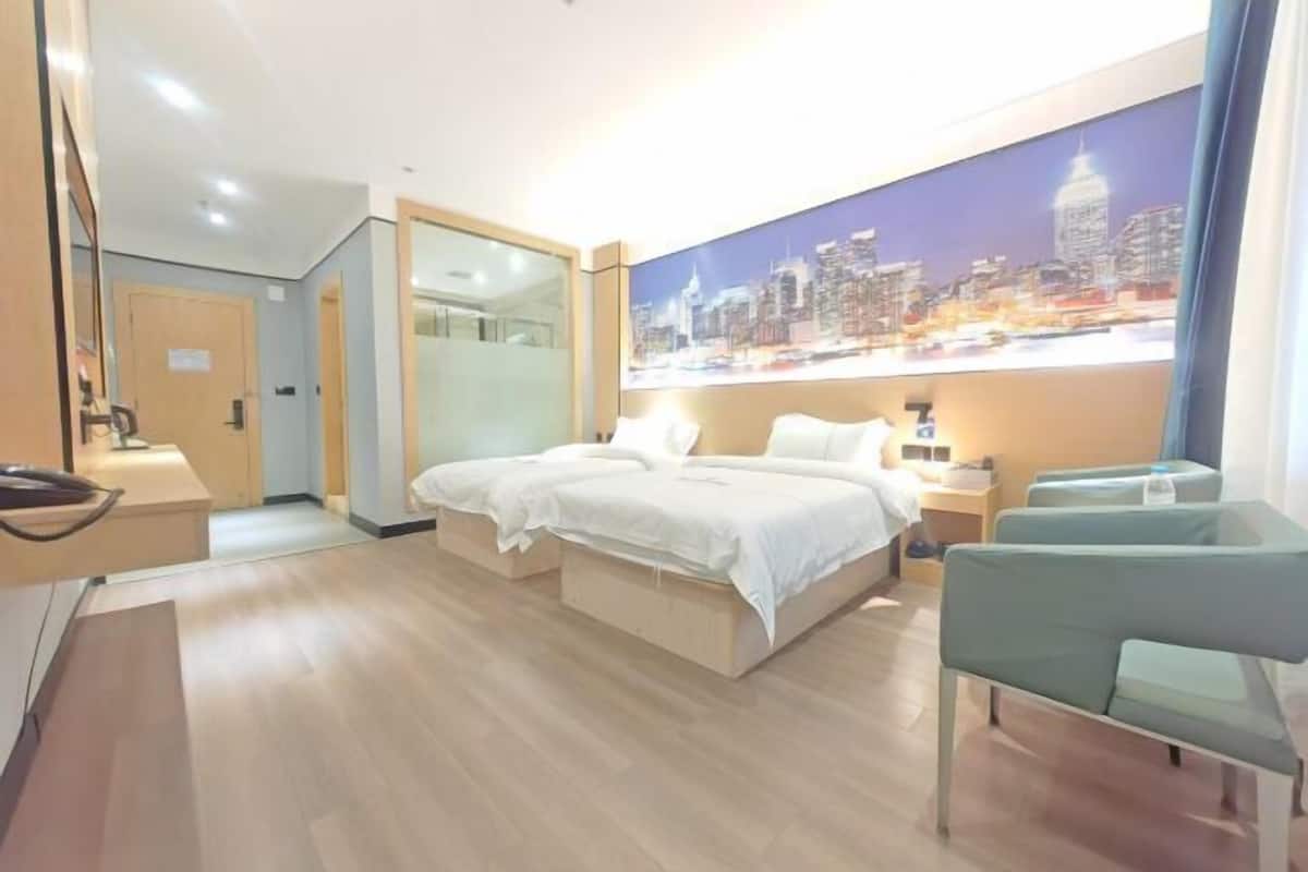 A hotel room with a bed, bedside tables, a desk, a chair, and a cityscape mural on the wall.