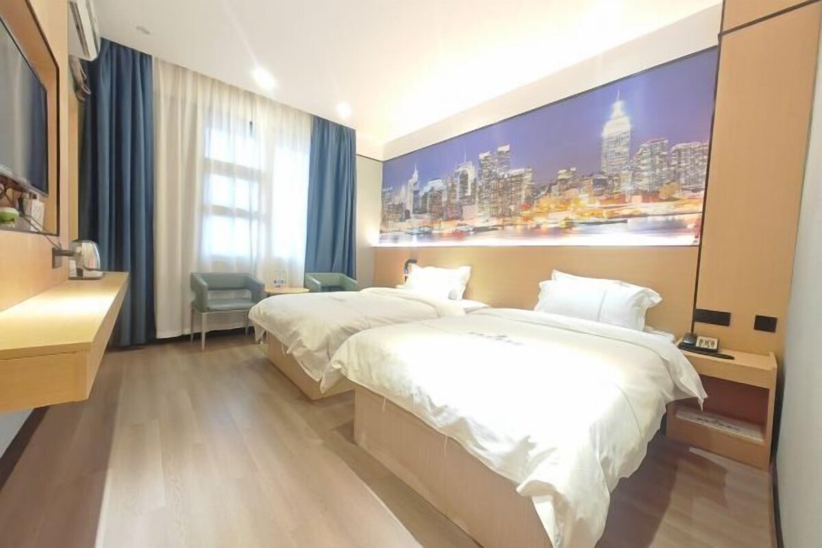 A hotel room with two beds, a desk, a chair, and a cityscape mural on the wall.