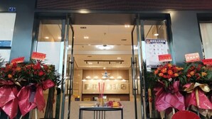 Entrada de un hotel con puertas de cristal, un mostrador de recepción y decoraciones florales.