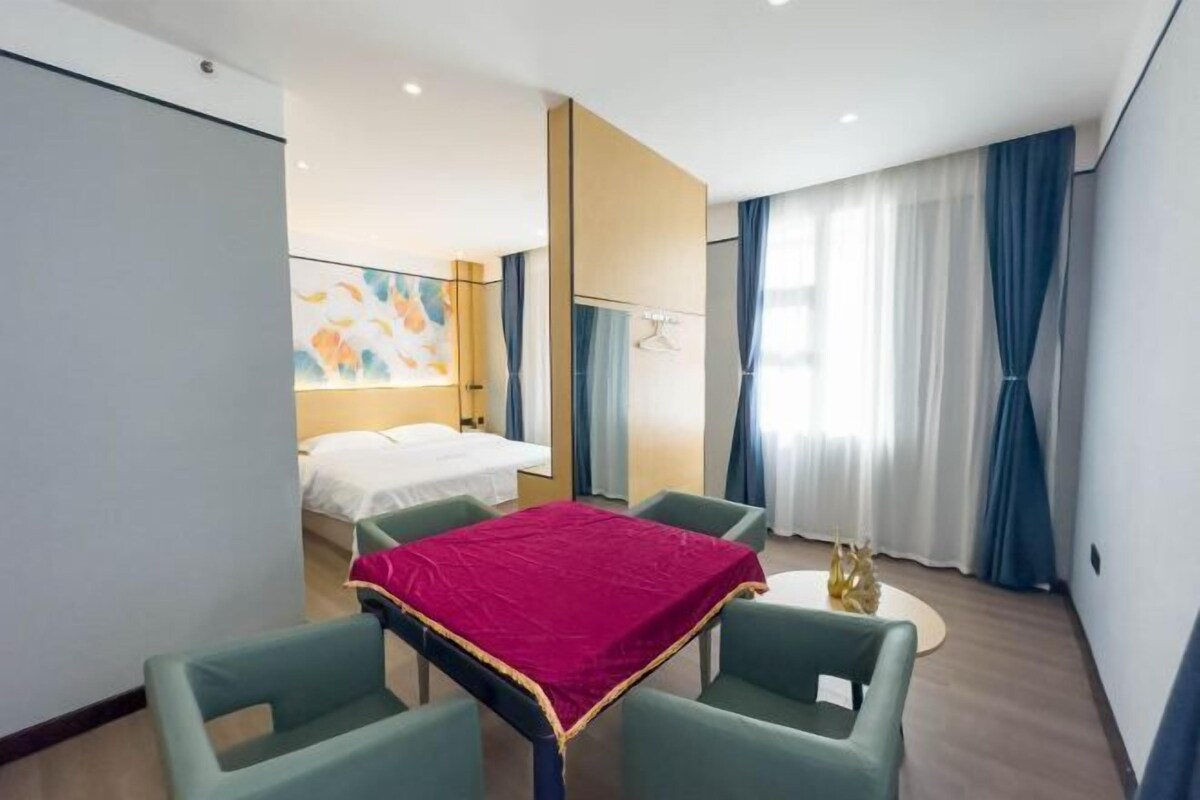 A modern hotel room with a bed, a dining table with chairs, a small round table with a decorative item, and a large abstract painting on the wall.