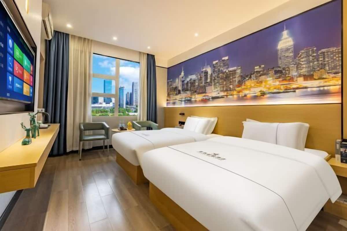 A hotel room with two beds, a desk, a large window with curtains, a painting of a cityscape, and a flat-screen TV on the wall.