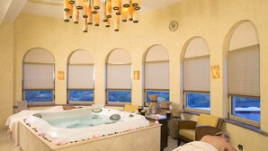 Um quarto de spa com uma banheira grande, janelas em arco e uma cama.