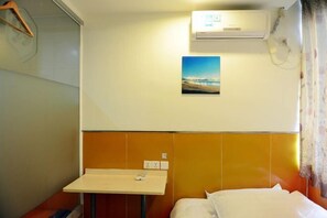 A hotel room with a bed, a small table with a remote control, an air conditioning unit, and a painting on the wall. - Ruixue Hostel (Shanghai Zhujing Zijin Plaza) (Shanghai)