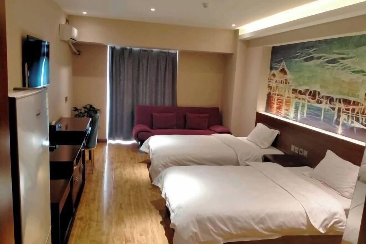 Habitación de hotel con dos camas, televisión, escritorio, sofá y un cuadro en la pared.