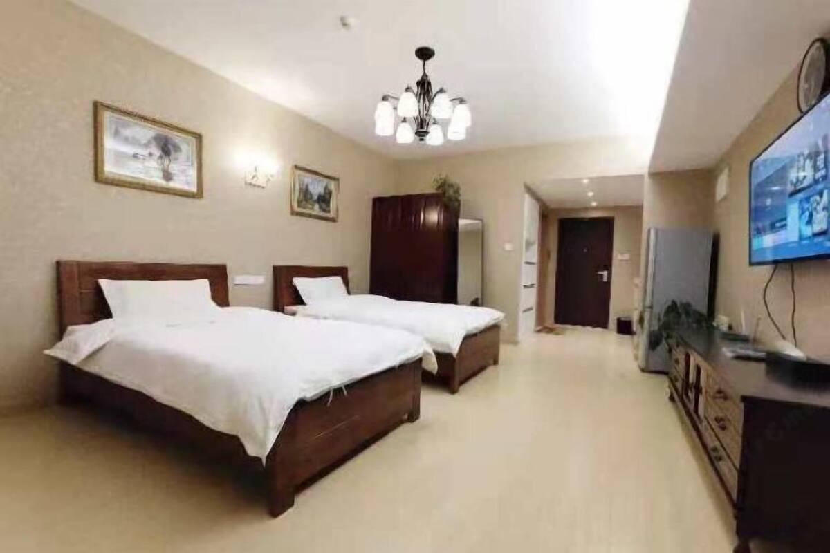 Habitación de hotel con dos camas, televisión, armario y candelabro.