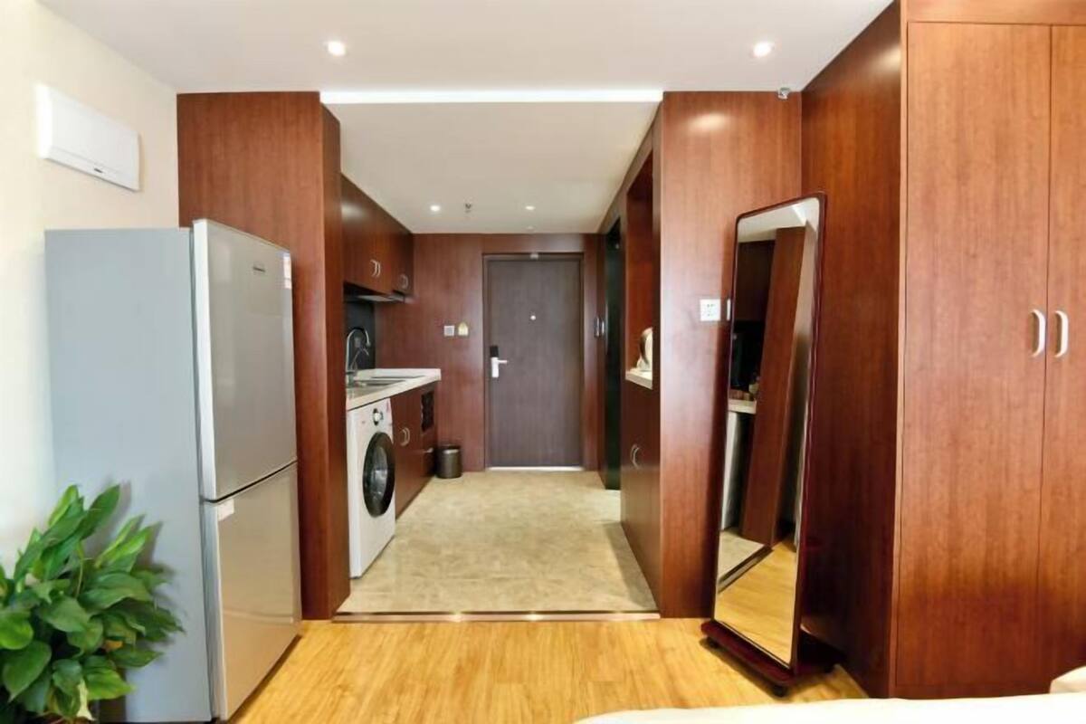 Habitación de hotel compacta con kitchenette, lavadora, espejo y suelo de madera.