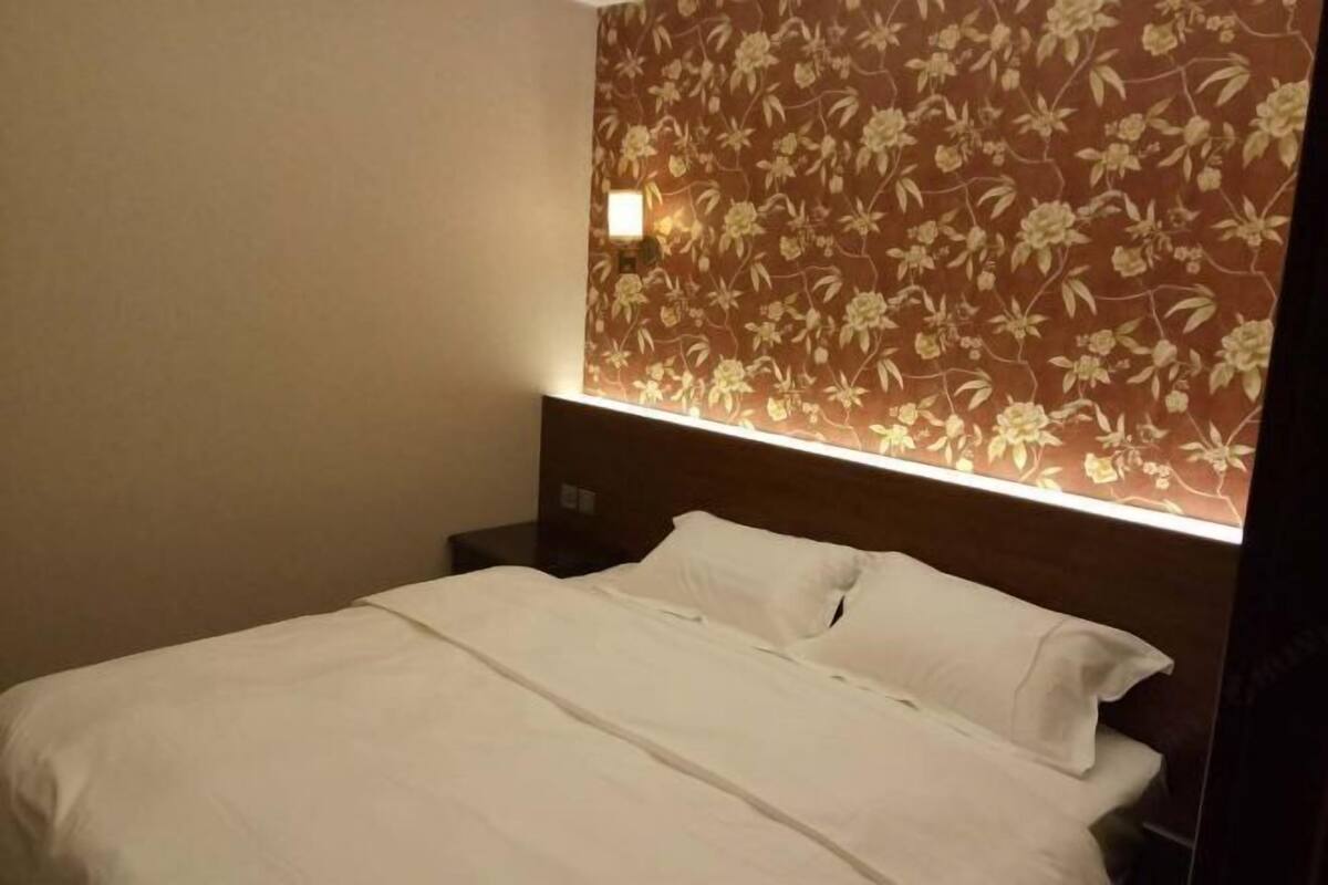 Habitación de hotel con cama, mesita de noche y papel tapiz con motivos florales.