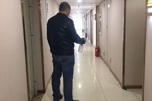 A man walking down a hallway with doors on both sides, a fire extinguisher on the right, and a clean, shiny floor.