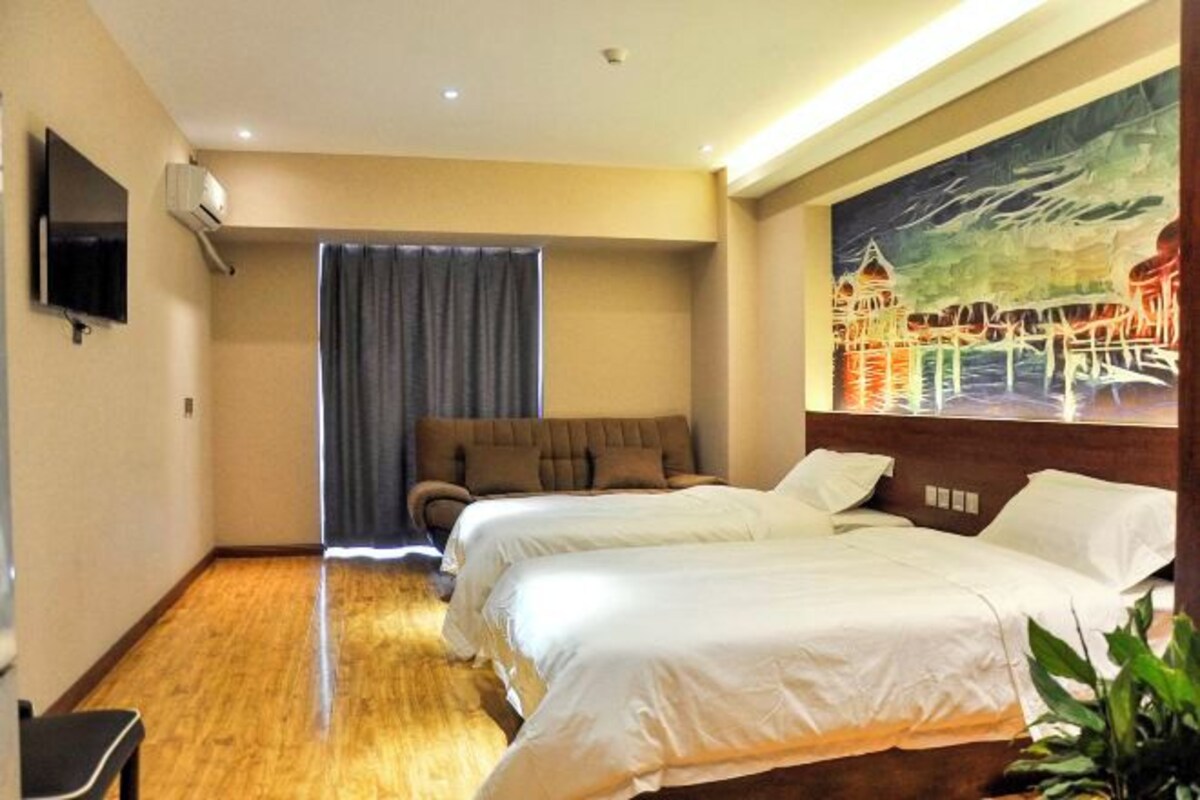 A hotel room with two beds, a flat-screen TV, a sofa, a painting, and a potted plant.