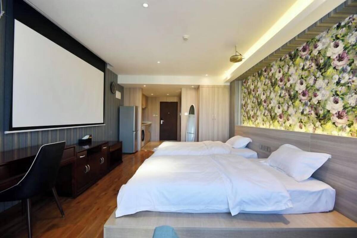 Habitación de hotel con cama, escritorio, silla, televisor y un papel tapiz floral.