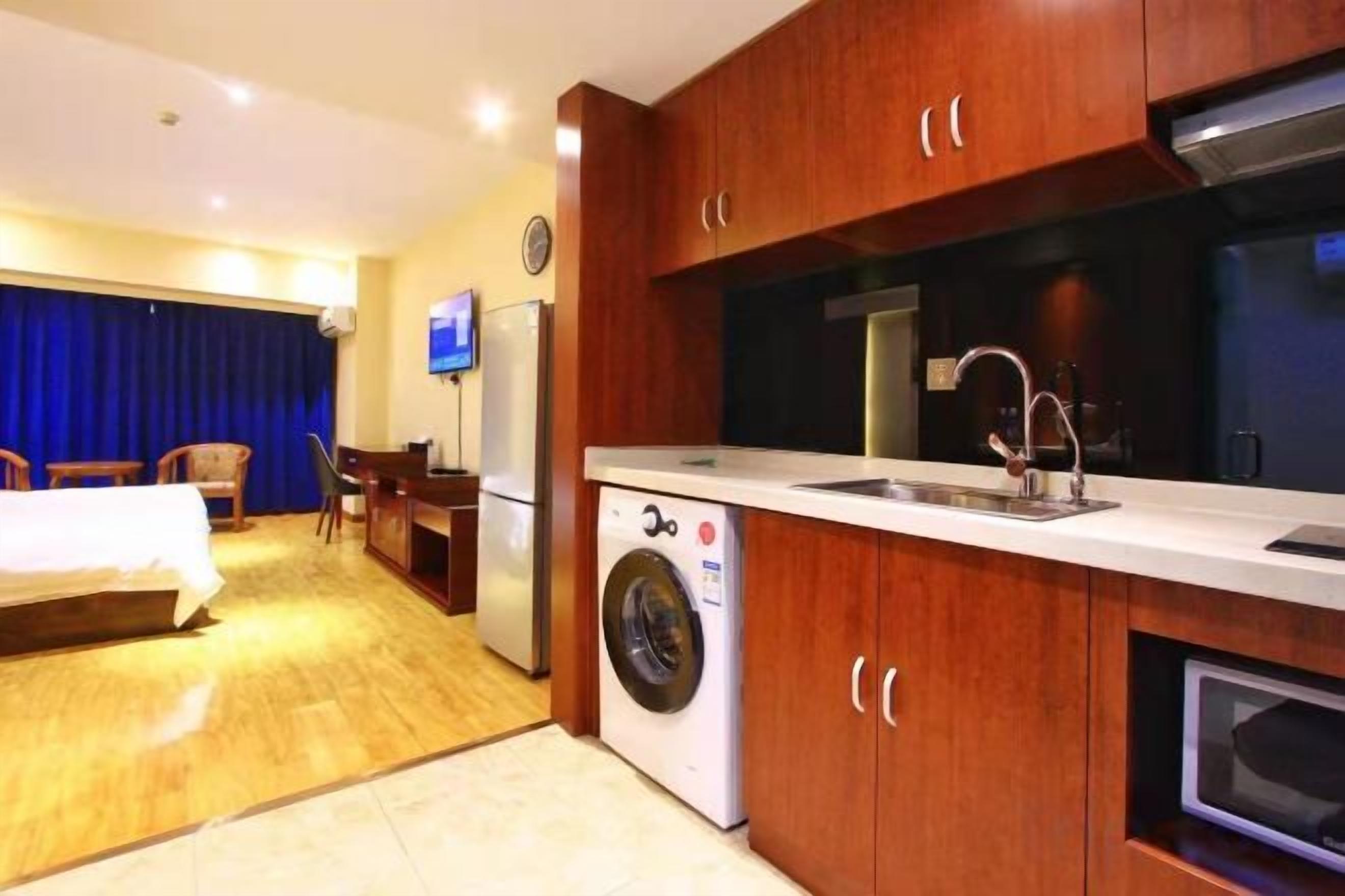 A hotel room with a bed, a desk, a washing machine, a kitchen area with a sink, and a television.