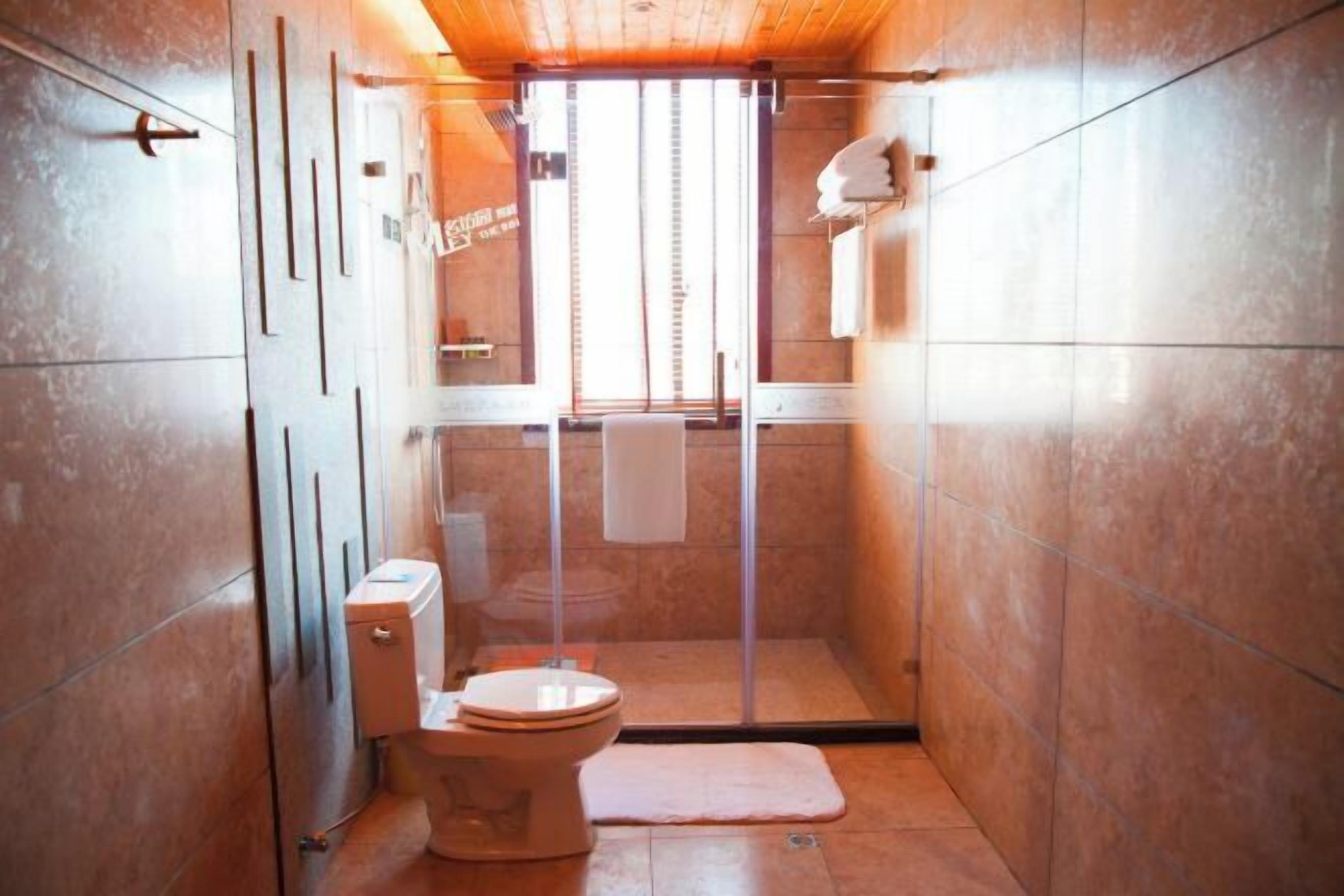Casa de banho compacta com sanita, cabine de duche em vidro e uma pequena janela.