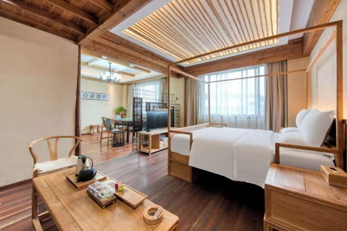Habitación de hotel con techo de madera, cama, escritorio con hervidor y zona de comedor con sillas y mesa.