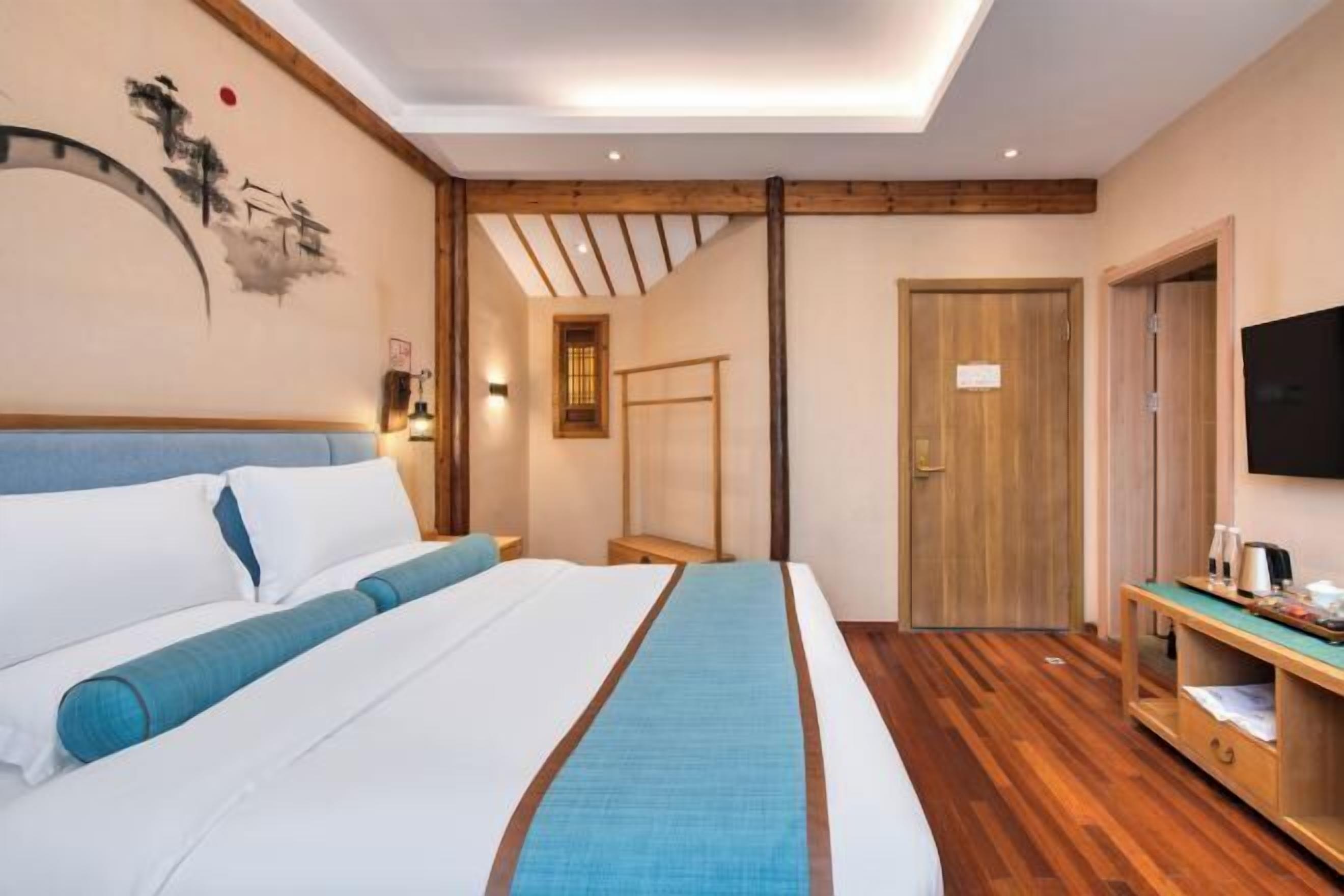Quarto de hotel com cama, piso de madeira, televisão e porta de madeira.