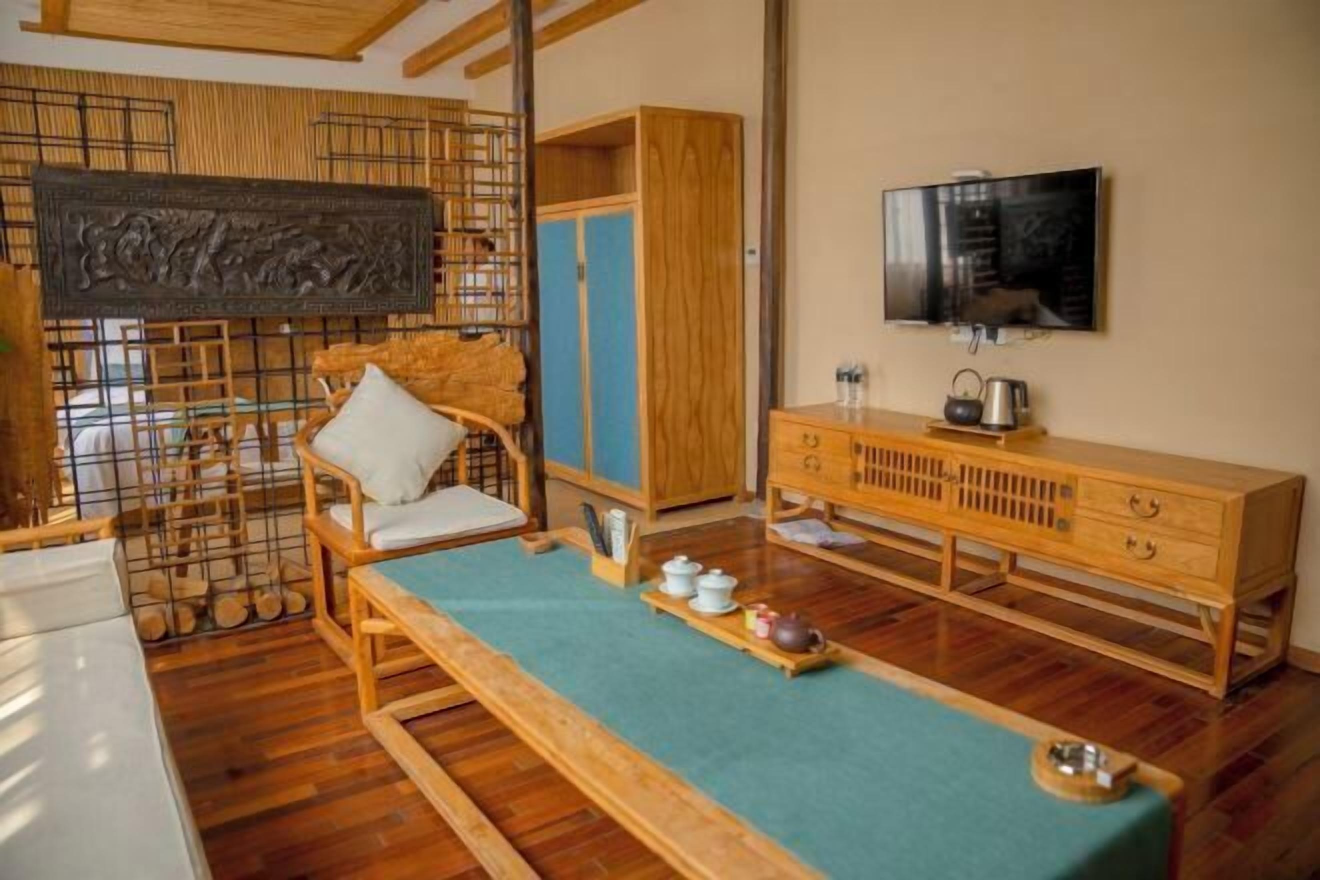 Um quarto tradicional japonês com tatames, uma mesa de madeira baixa com um conjunto de chá, uma televisão na parede e um armário de madeira.