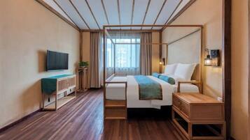 A modern hotel room with a wooden floor, a bed with a wooden frame, a bedside table, a TV on the wall, and a window with curtains.