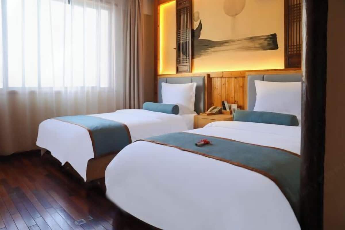 Habitación de hotel con dos camas, suelo de madera, una mesita de noche con teléfono y un cuadro en la pared.