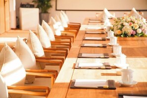 Een vergaderzaal met een lange tafel gedekt voor een vergadering, voorzien van stoelen, tafels en een bloemstuk.