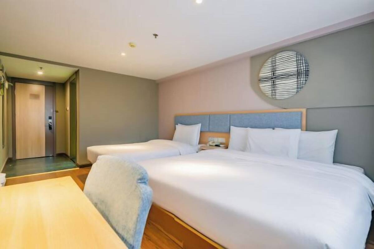 A hotel room with two beds, a round wall clock, and a wooden floor.