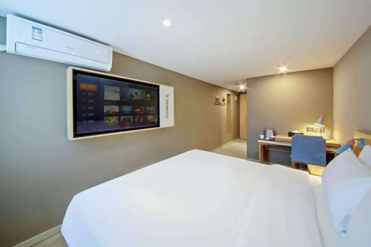 A hotel room with a bed, a desk, and a wall-mounted TV.