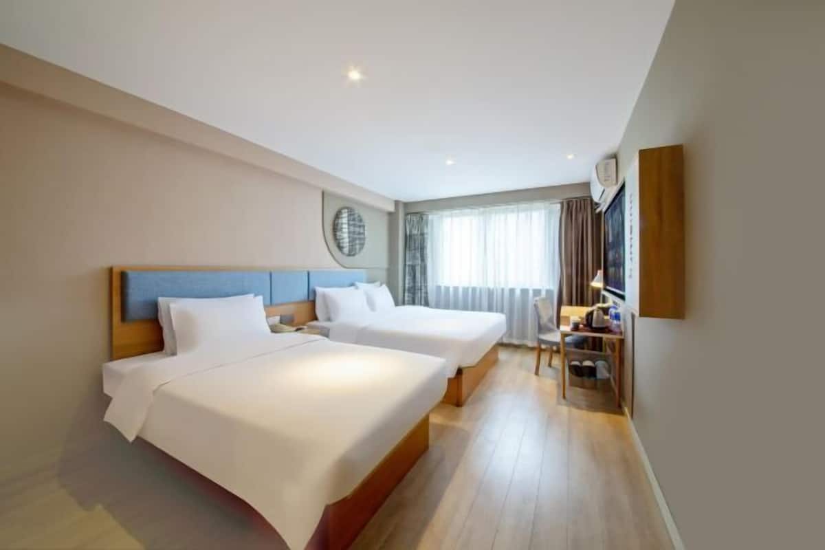 A hotel room with two beds, a desk, a chair, and a large window with curtains.