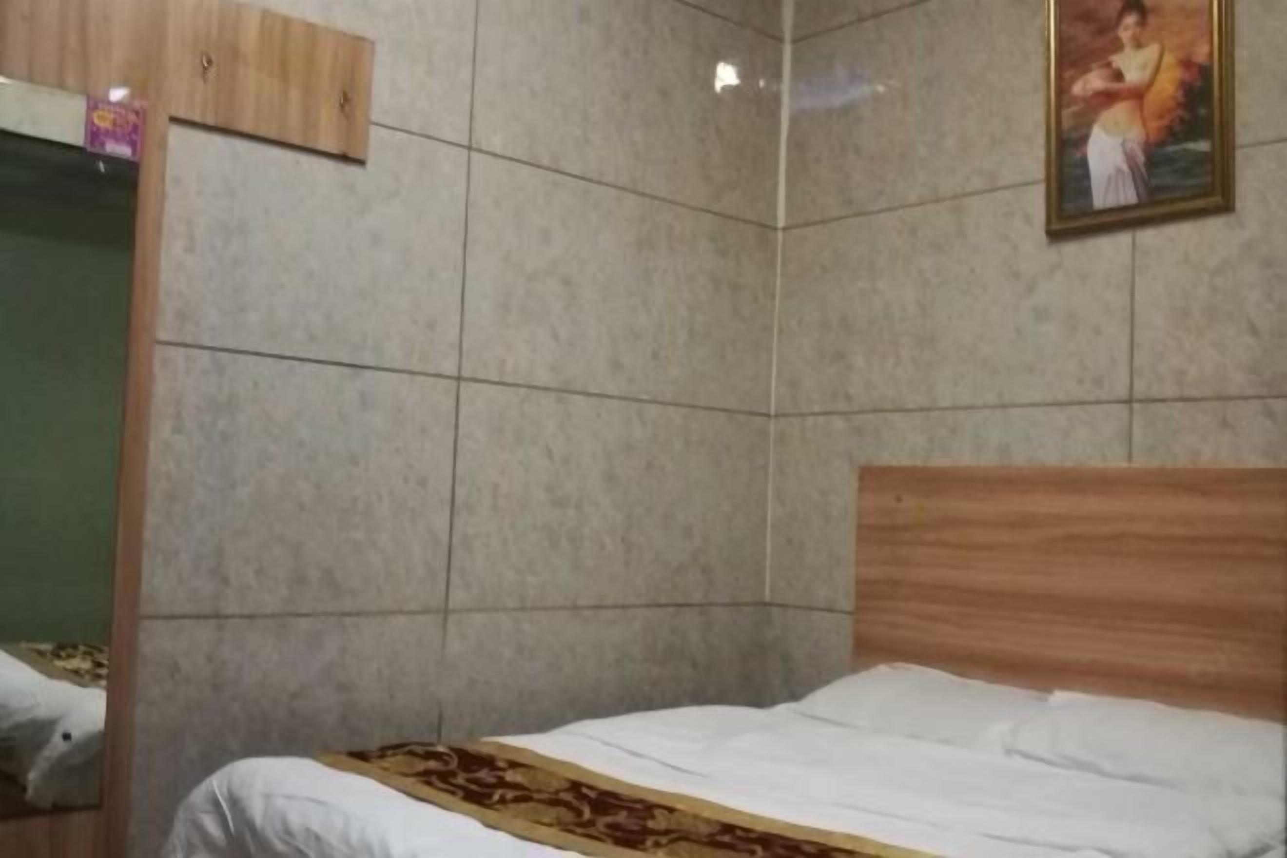 A room with a bed, a wooden headboard, a tiled wall, and a framed picture on the wall.