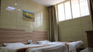 Ein Hotelzimmer mit zwei Betten, einem hölzernen Kopfteil, einem Bild an der Wand und einem Fenster mit Vorhängen.