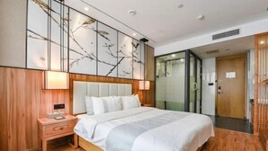 A modern hotel room with a large bed, wooden paneling, a nightstand, a wall-mounted artwork, and a sliding door leading to another room. - Riyue Lake Culture Hotel (Shangqiu)