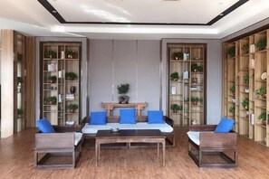 A spacious living area with a sofa set, a coffee table, and a bookshelf filled with books and plants. - Riyue Lake Culture Hotel (Shangqiu)