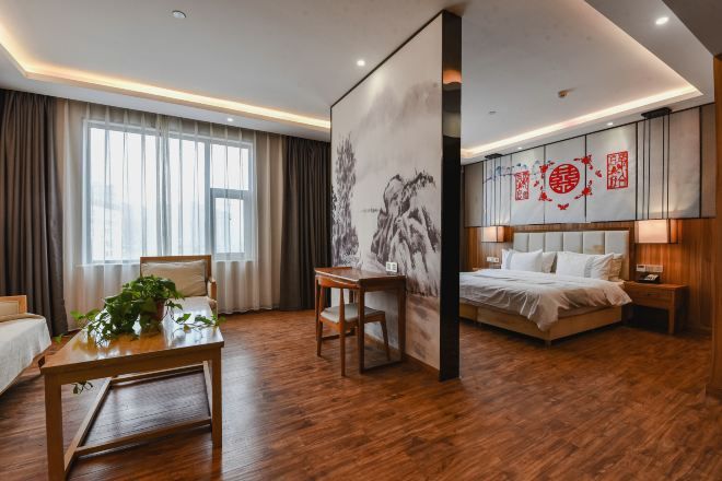 Een hotelkamer met een houten vloer, een bed met wit beddengoed, een bureau met een plant en een groot schilderij aan de muur.
