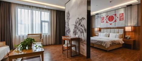 A hotel room with a wooden floor, a bed with white bedding, a desk with a plant, and a large painting on the wall.