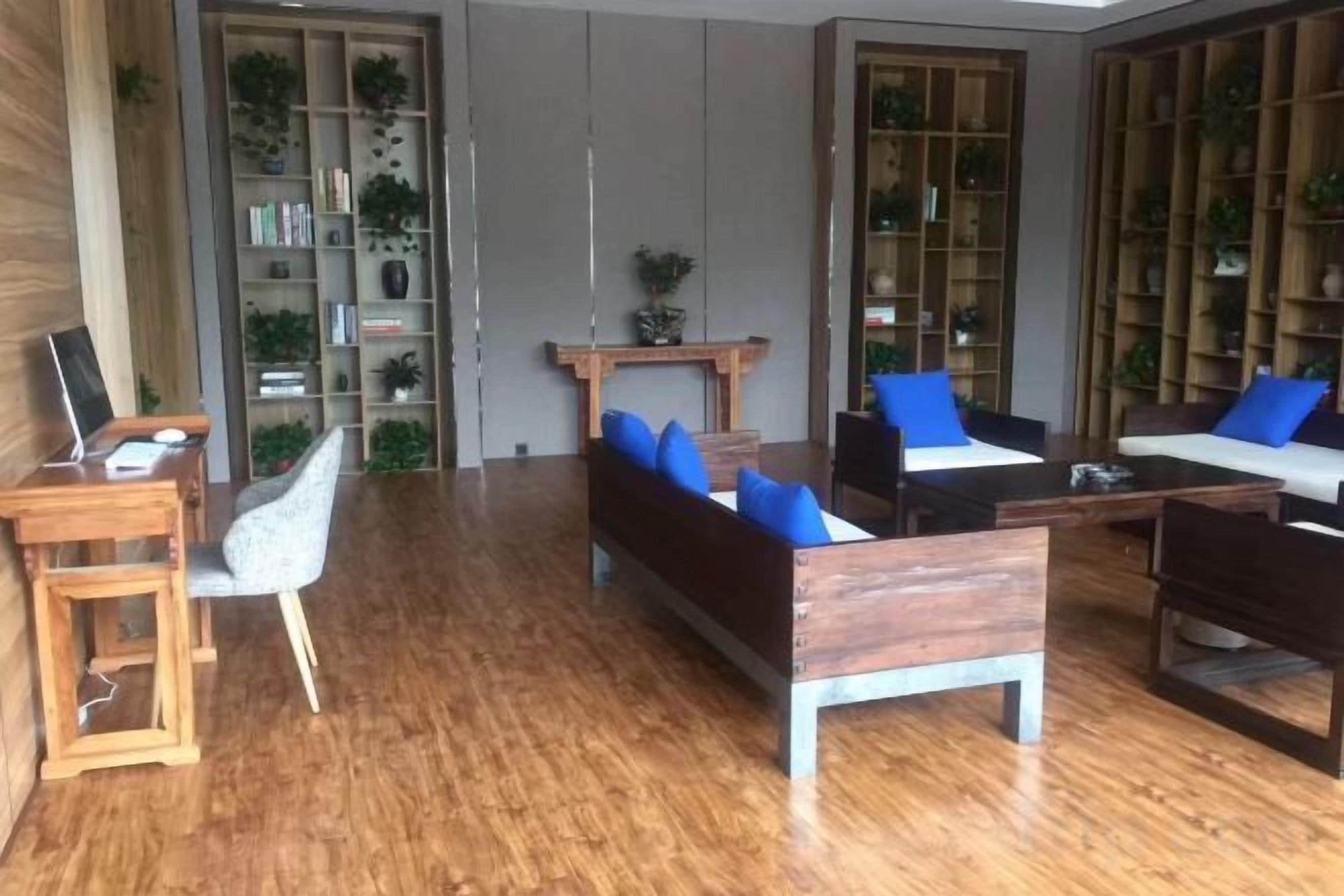 A modern living room with a wooden floor, a sofa with blue cushions, a coffee table, and a bookshelf filled with books and plants.