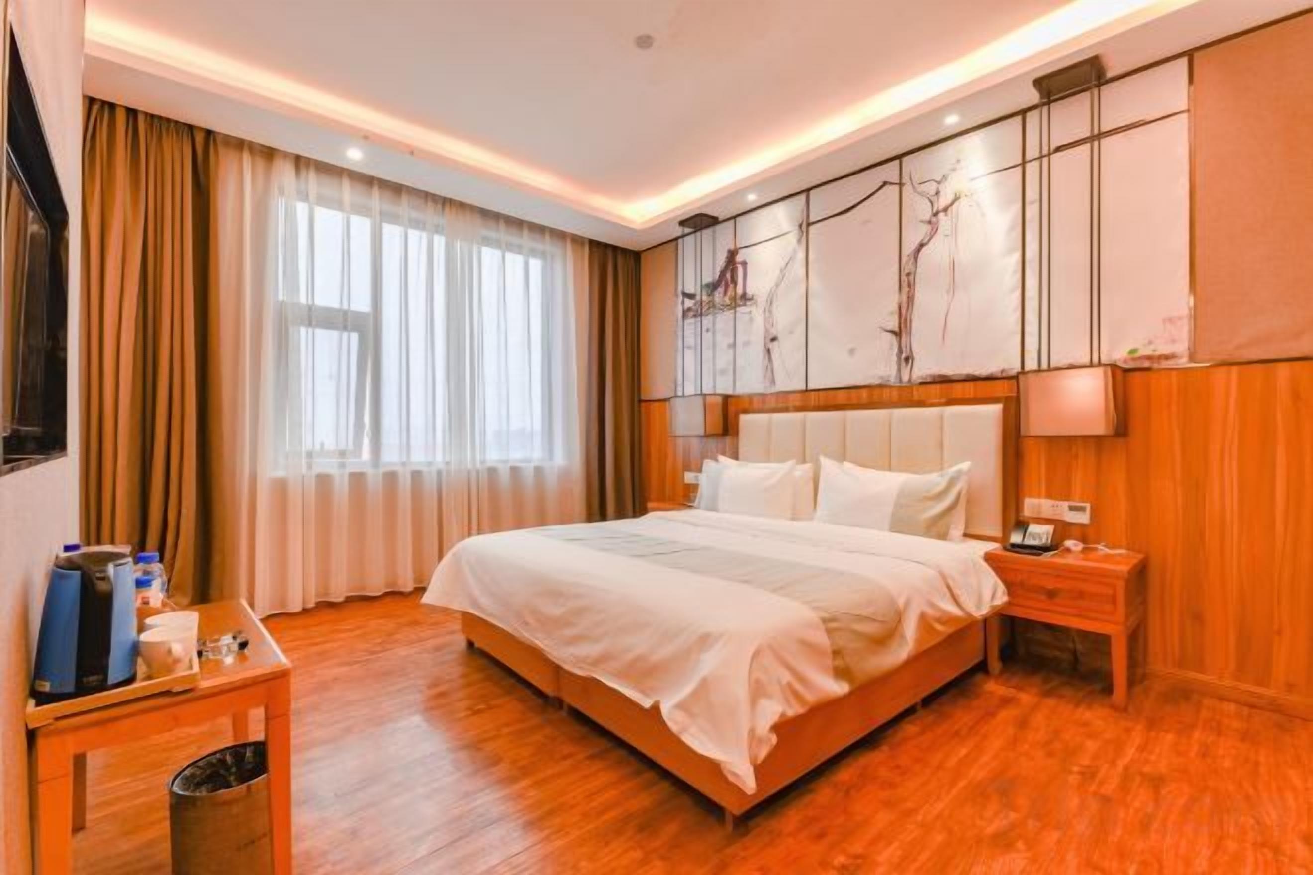 A hotel room with a large bed, bedside tables, a wooden floor, and a window with curtains.