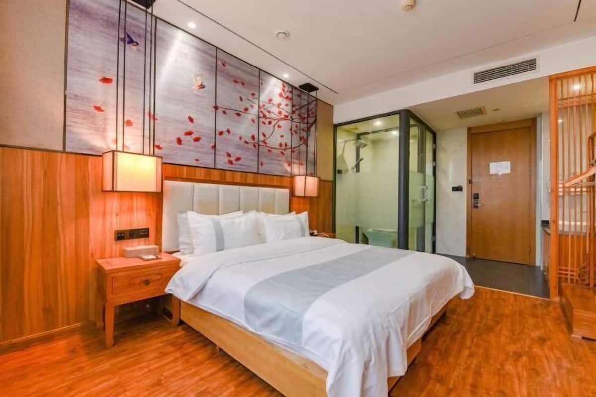 A hotel room with a wooden floor, a bed with white bedding, a nightstand, a wall-mounted artwork, and a sliding door leading to a bathroom.