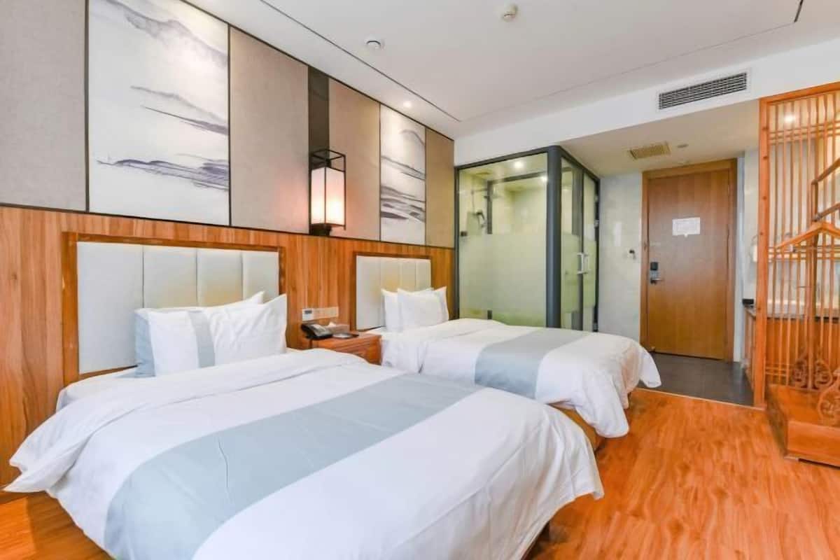 A hotel room with two beds, a wooden headboard, a wall-mounted lamp, and a glass shower enclosure.