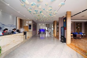 A hotel lobby with a reception desk, seating area, and a large screen.