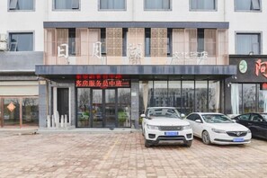 Un hotel con fachada moderna, una entrada visible y un estacionamiento con coches.