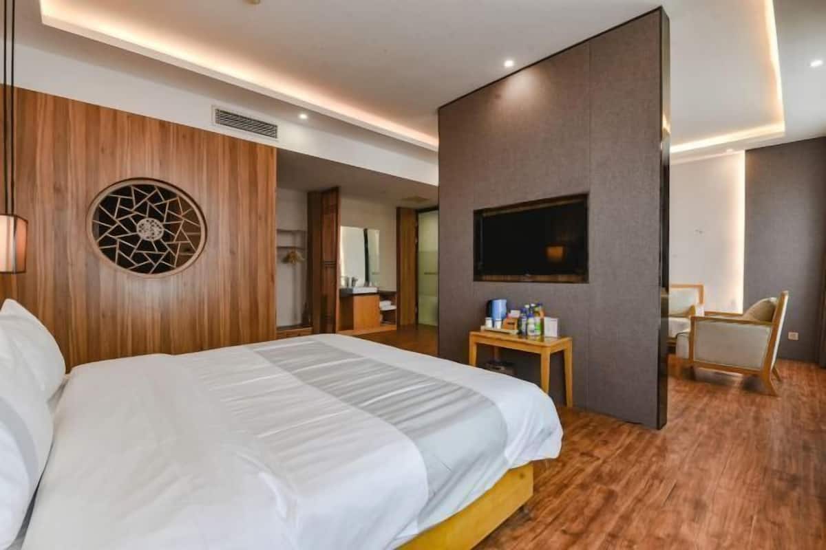 A modern hotel room with a large bed, a TV mounted on the wall, a wooden accent wall, and a small table with toiletries.