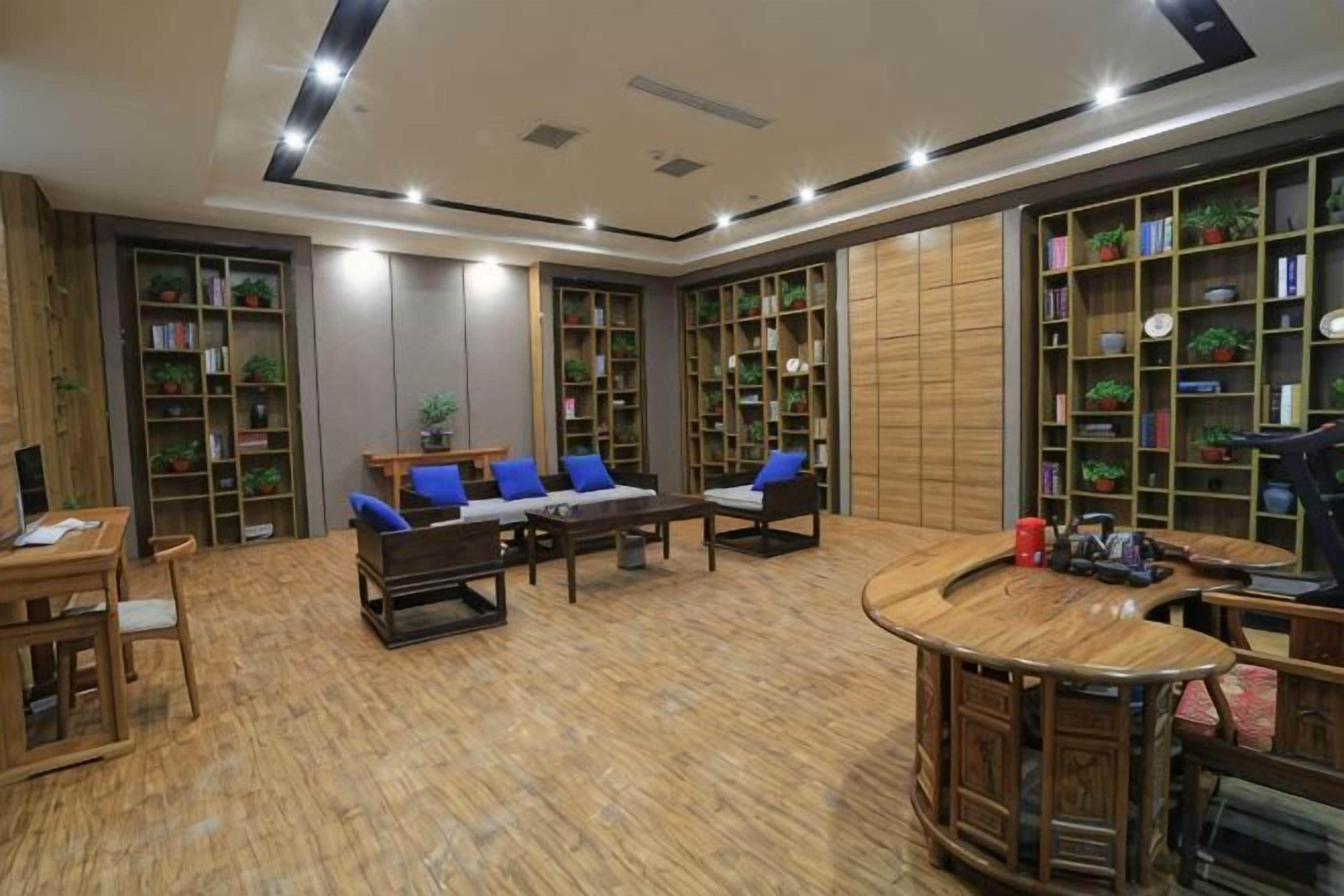 A spacious room with a wooden floor, a sofa set, a dining table, and multiple bookshelves filled with books and plants.