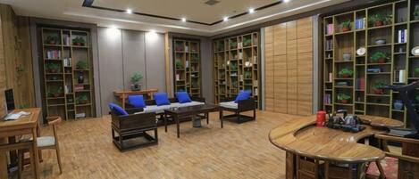 A spacious room with a wooden floor, a sofa set, a dining table, and multiple bookshelves filled with books and plants.