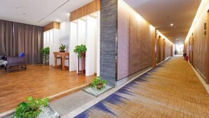 A hotel corridor with wooden flooring, a reception area with a desk and chairs, and a wall with a textured pattern. - Riyue Lake Culture Hotel (Shangqiu)