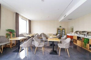 A dining area with tables and chairs, a buffet station, and a plant. - Riyue Lake Culture Hotel (Shangqiu)