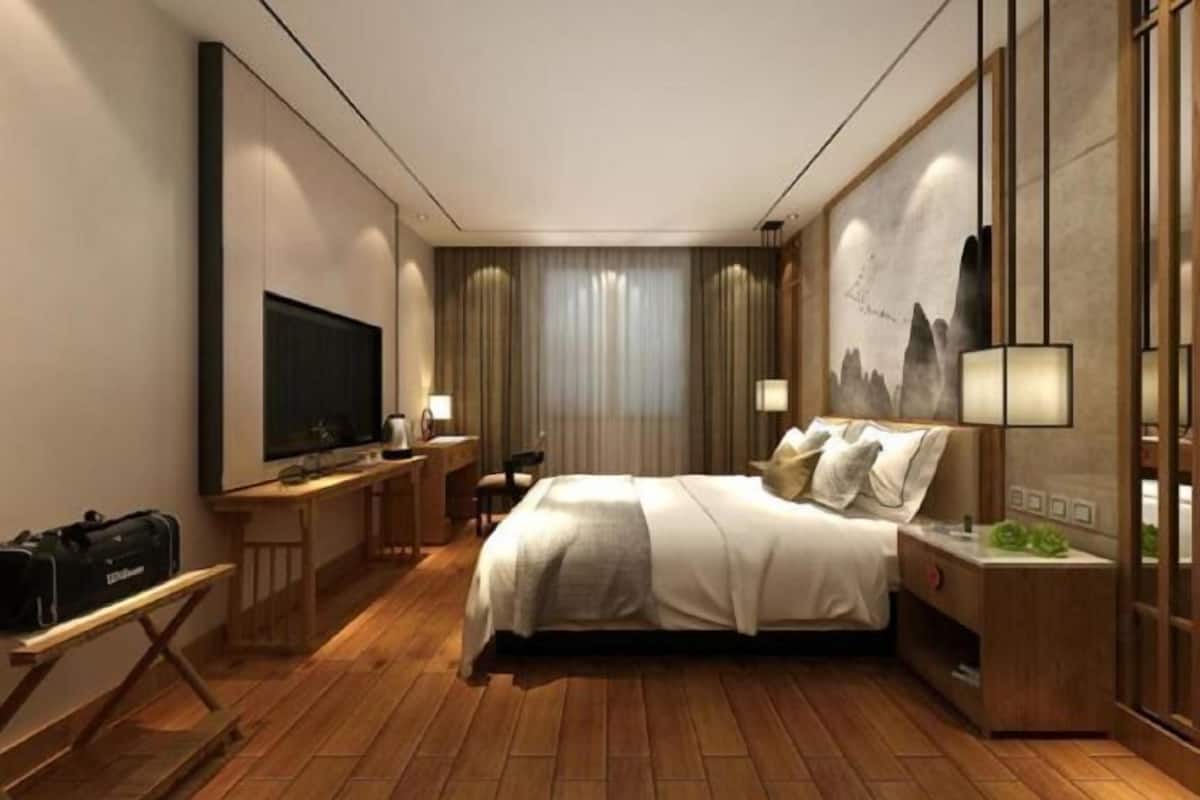 A hotel room with a bed, desk, TV, and a painting on the wall.