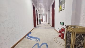 A hotel corridor with patterned carpet, fire extinguishers, and a fire alarm on the wall.