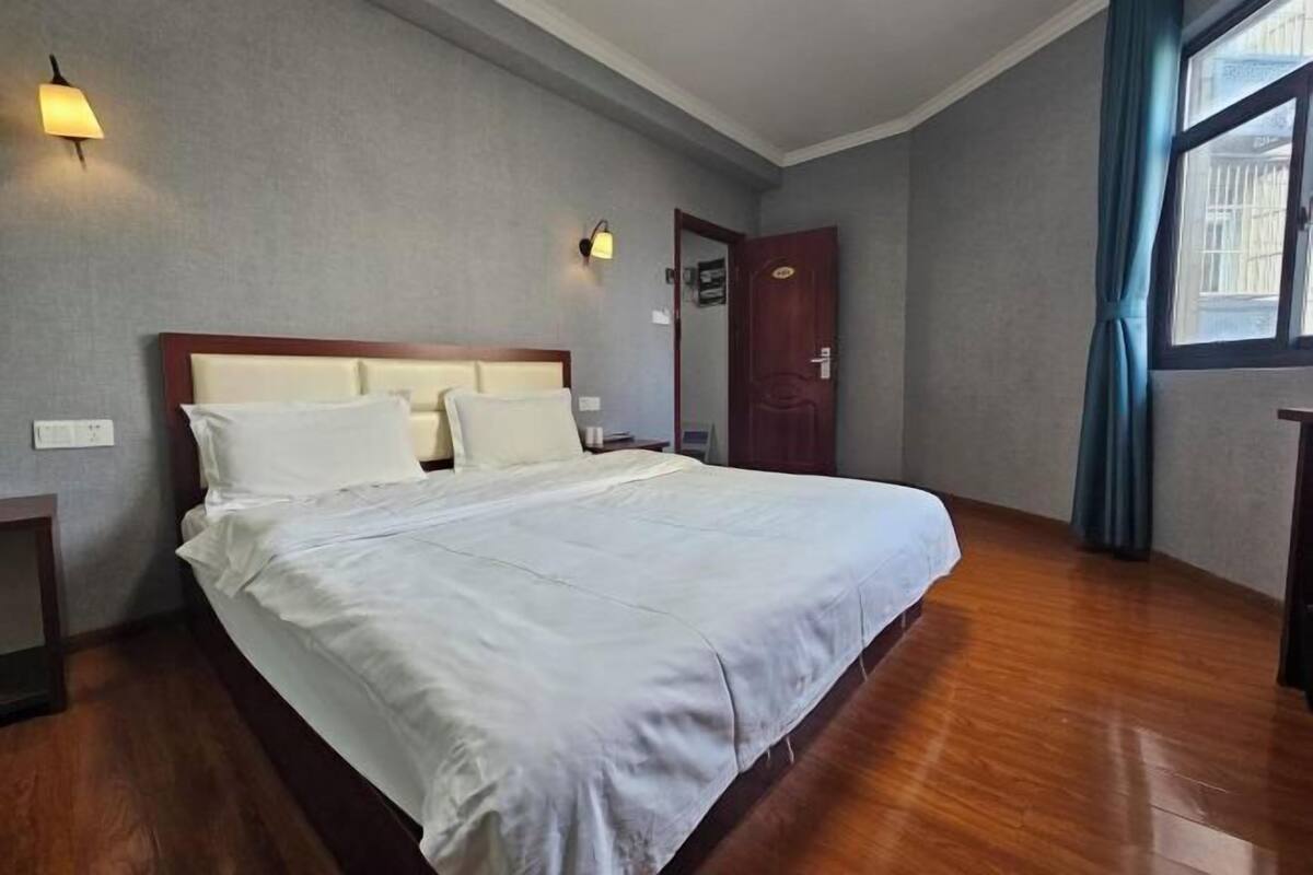 Hotellihuone, jossa on suuri sänky, puulattia, ovi ja ikkuna, jossa on verhot.