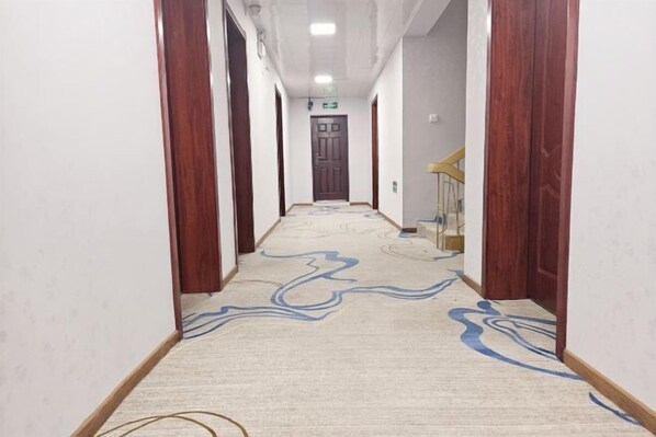 A hallway with a patterned carpet, wooden doors, and a staircase. - Nanjing Ruijia Hotel (Yuhuatai Scenic Area Branch) (Nanjing)
