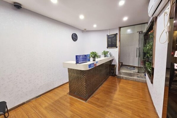 Uma área de recepção com piso de madeira, um balcão de atendimento com design estampado, um relógio na parede e uma porta de vidro que dá para uma área de chuveiro.